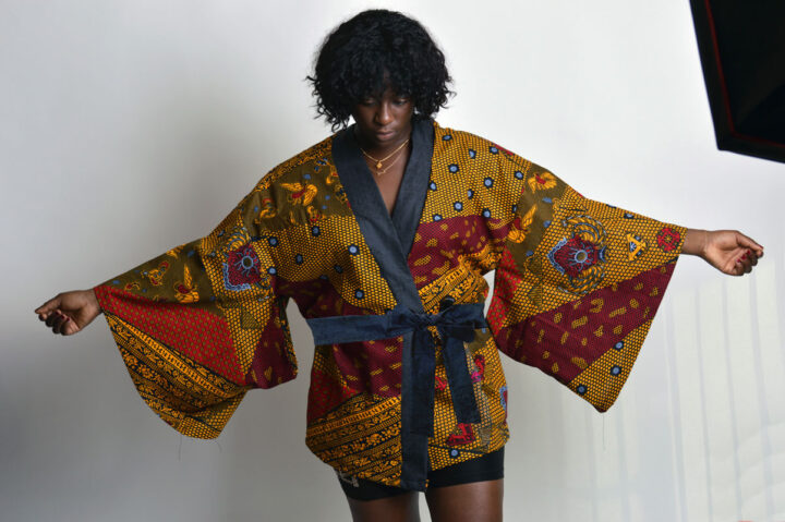 model with arm stretched showing an african print kimono with with japanese style sleeves black strip on the v neck and black belt